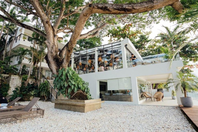Terraza acristalada del restaurante con jardín tropical y árbol centenario en Solitude Acacia Resort