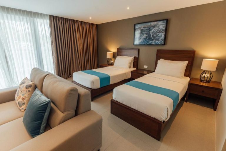 Habitación twin con dos camas y sofá en Solitude Acacia Resort, decoración moderna en tonos azules