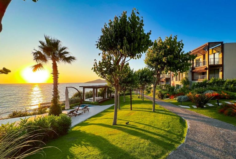 Jardines con vistas al mar al atardecer en el Allium Bodrum Resort & Spa con tumbonas y palmeras
