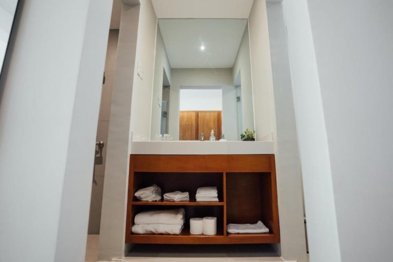 Baño moderno con lavabo empotrado, estantes de madera y toallas blancas en Solitude Acacia Resort