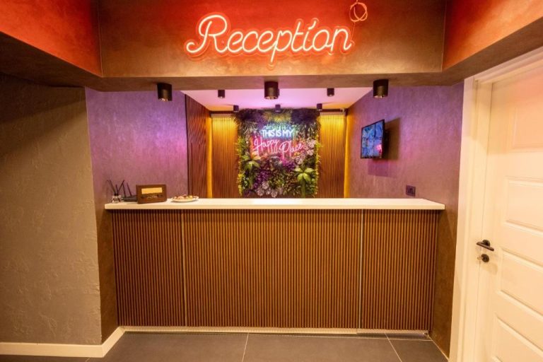Recepción moderna con letrero de neón del Comfort House Hotel decorada con plantas y ambiente colorido