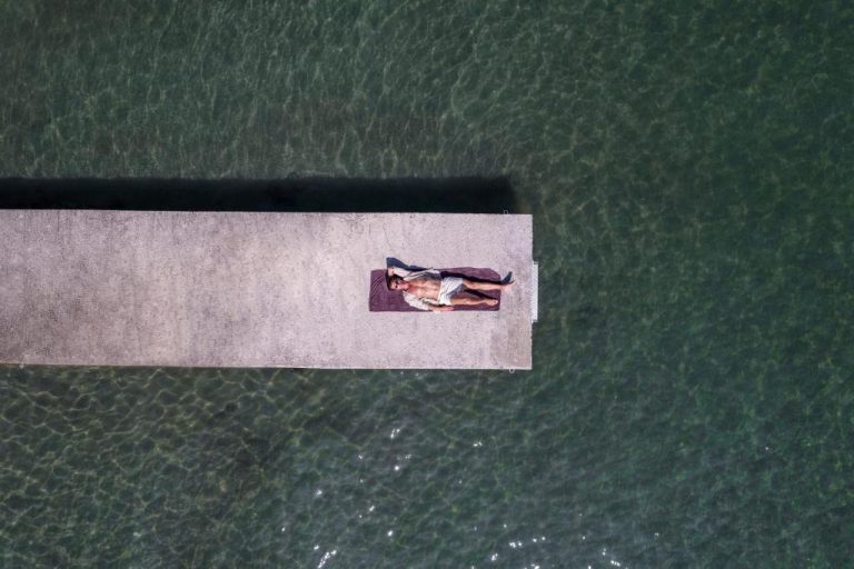 Turista tomando el sol en el embarcadero del Kerkyra Blue Hotel & Spa by Louis Hotels con aguas cristalinas