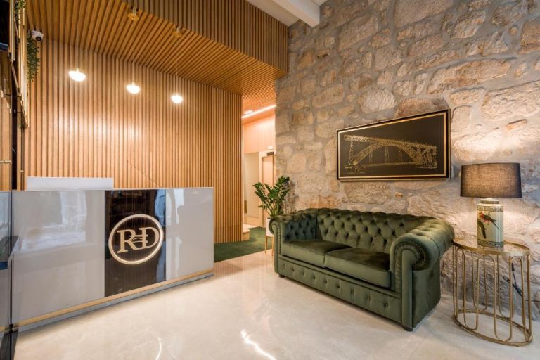 Recepción elegante con sofá Chesterfield verde y pared de piedra en Ribeira Douro Hotel