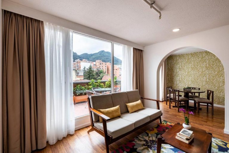 Sala de estar con sofá y gran ventanal con vista a la montaña en Hotel Vilar América Bogotá