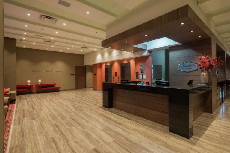 Recepción y lobby moderno del Hampton by Hilton Bogotá Airport con mostrador de check-in y suelos de madera
