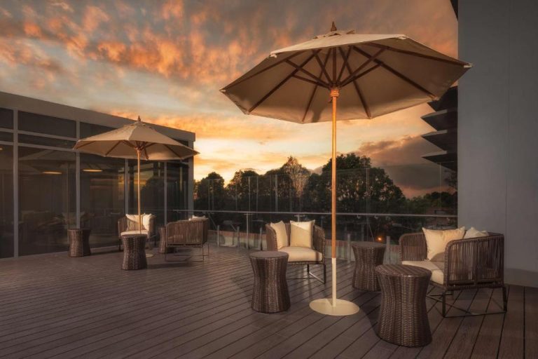 Terraza exterior con sillas de mimbre y sombrillas al atardecer en Hilton Garden Inn Bogotá Airport