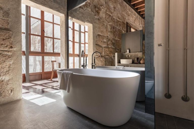 Lujoso baño con bañera exenta blanca y paredes de piedra natural en Nobis Hotel Palma Design Hotels