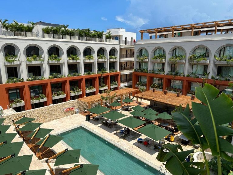 Piscina exterior con tumbonas y sombrillas verdes en el Osh Hotel Cartagena rodeada de vegetación tropical
