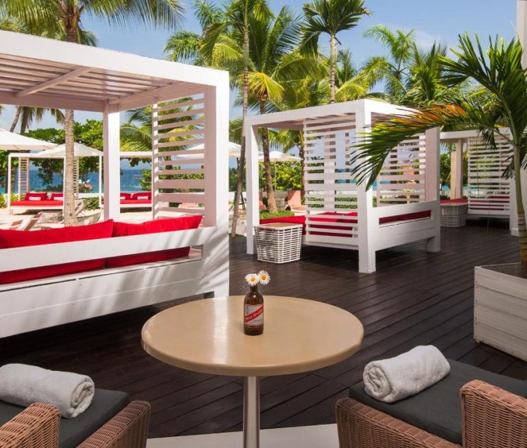 Cabanas de lujo con cojines rojos en terraza de madera del S Hotel Montego Bay frente a la playa