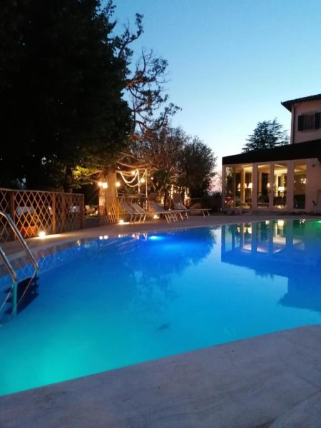 Piscina exterior iluminada de noche en Cortona Resort & Spa con vistas al jardín y terraza
