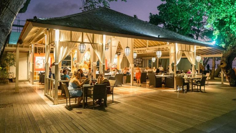 Terraza del restaurante iluminada por la noche en el Bali Garden Beach Resort con mesas al aire libre