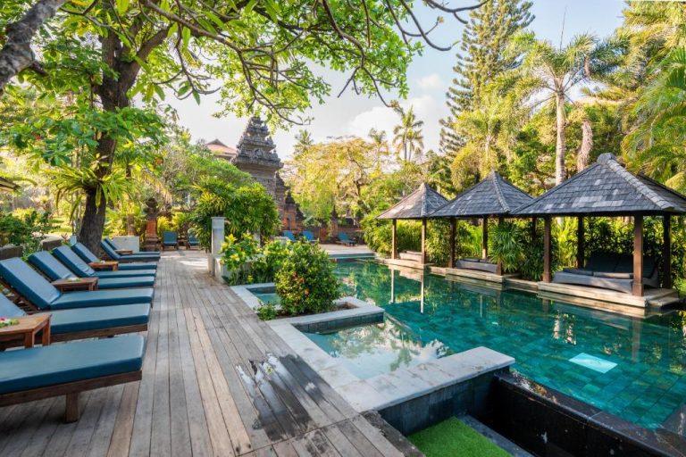 Piscina exterior con tumbonas y gazebos rodeada de jardín tropical en Bali Garden Beach Resort