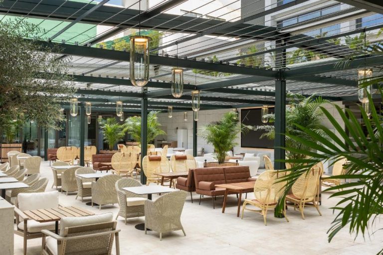 Terraza exterior con mesas y sillones de ratán del EVOLUTION Cascais-Estoril Hotel rodeada de palmeras