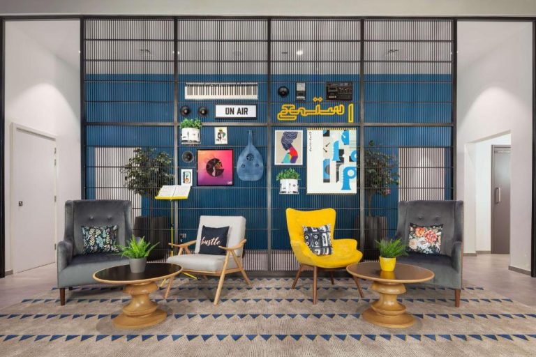 Zona social del lobby en Rove City Walk con decoración musical, sillones coloridos y pared azul con arte urbano