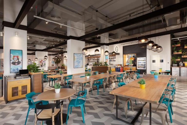 Restaurante interior del Rove City Walk con mesas de madera, sillas turquesa y decoración industrial moderna