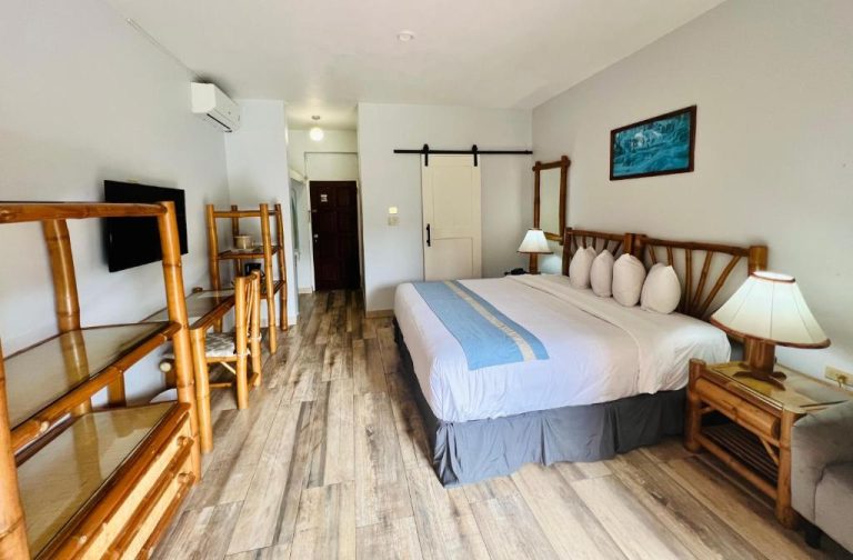Habitación doble con cama king, muebles de bambú y suelo de madera en Toby's Resort