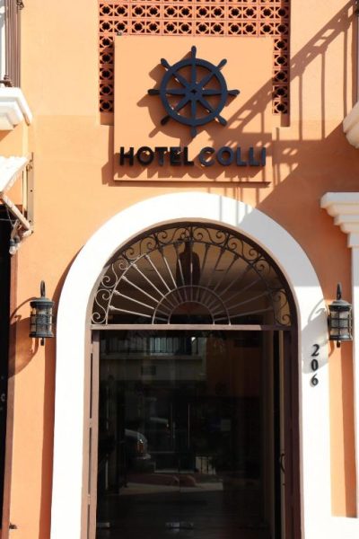 Fachada y entrada principal del Hotel Colli con arco decorativo y logo náutico en color naranja