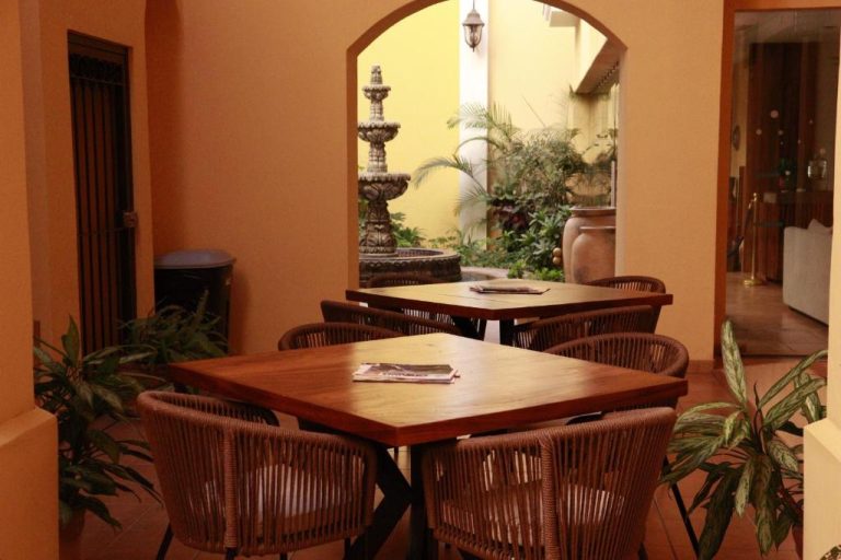 Restaurante interior del Hotel Colli con mesas de madera y patio con fuente decorativa y plantas tropicales