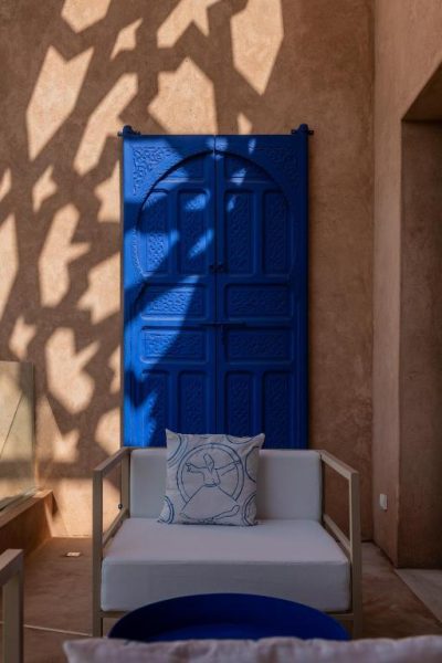 Puerta azul tallada de estilo marroquí con sillón exterior en Maison Kenoosha Boutique Hotel & Spa