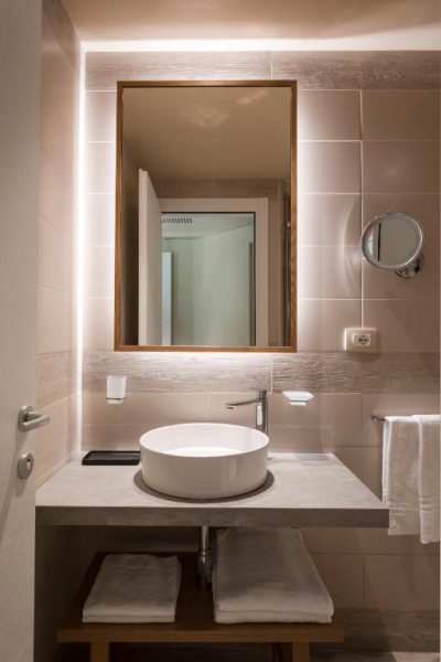 Baño moderno con lavabo de porcelana y espejo retroiluminado en Mangia's Brucoli Autograph Collection