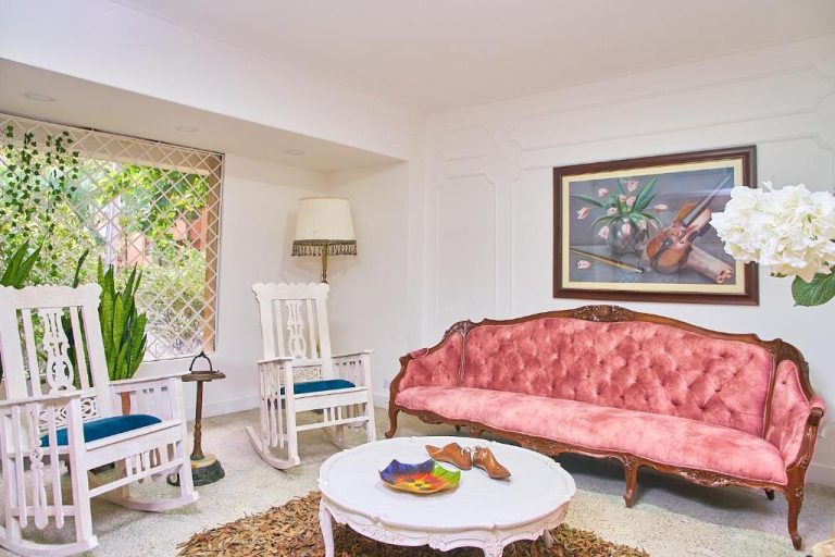 Elegante sala de estar clásica con sofá rosa tufted y sillas mecedoras blancas en Hotel Boutique Fiorentina Medellín