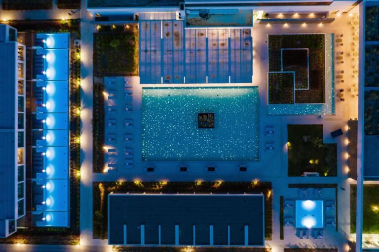 Vista aérea nocturna de la piscina iluminada del Gennadi Grand Resort con tumbonas y jardines