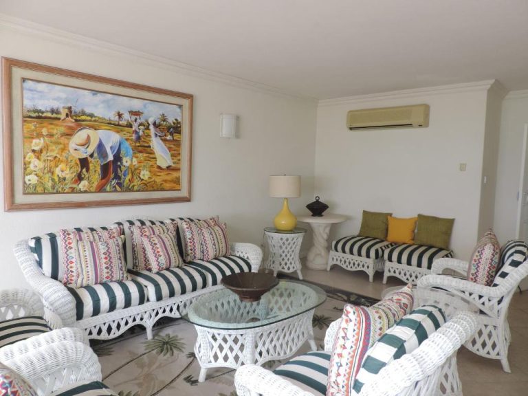 Sala de estar con muebles de mimbre blanco y decoración caribeña en Coral Sands Beach Resort