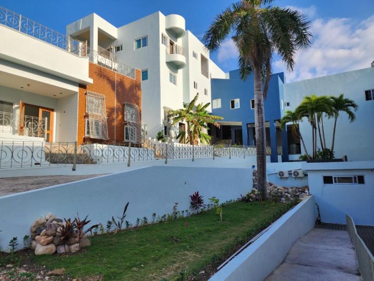 Fachada exterior del Hotel 39 Jamaica con piscina, jardines tropicales y palmeras bajo cielo azul