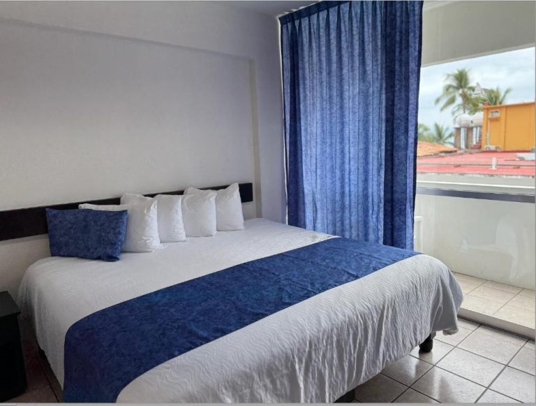 Habitación con cama doble y cortinas azules con vista exterior en Delfin Beachfront Resort Puerto Vallarta