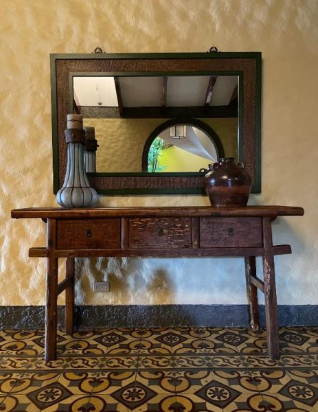 Consola de madera antigua con espejo y decoración colonial en el Hotel 1915 Inn & Suites