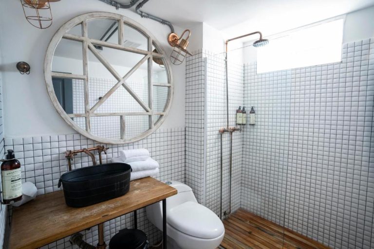 Baño de estilo industrial con lavabo negro, ducha de cobre y azulejos blancos en Hotel Kim