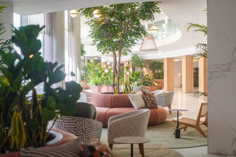 Luminoso lobby del DoubleTree by Hilton Malta con sofás rosas, árboles naturales y decoración tropical