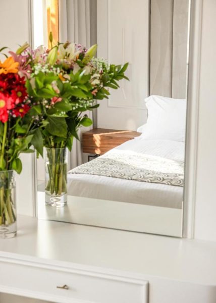 Tocador blanco con flores coloridas y espejo que refleja la cama del Hotel Bella Venezia