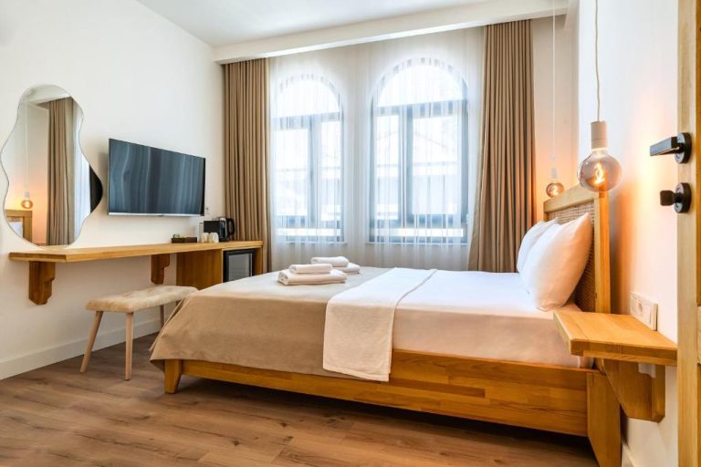Habitación doble con cama de madera, TV y ventanas en arco del Hotel Audo Local