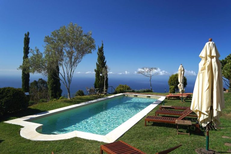Piscina exterior con tumbonas y vistas al mar del Hotel Atrio rodeada de jardín y cipreses