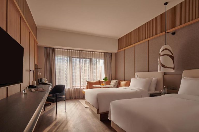 Habitación twin moderna con dos camas y sofá en tonos cálidos del Amara Singapore
