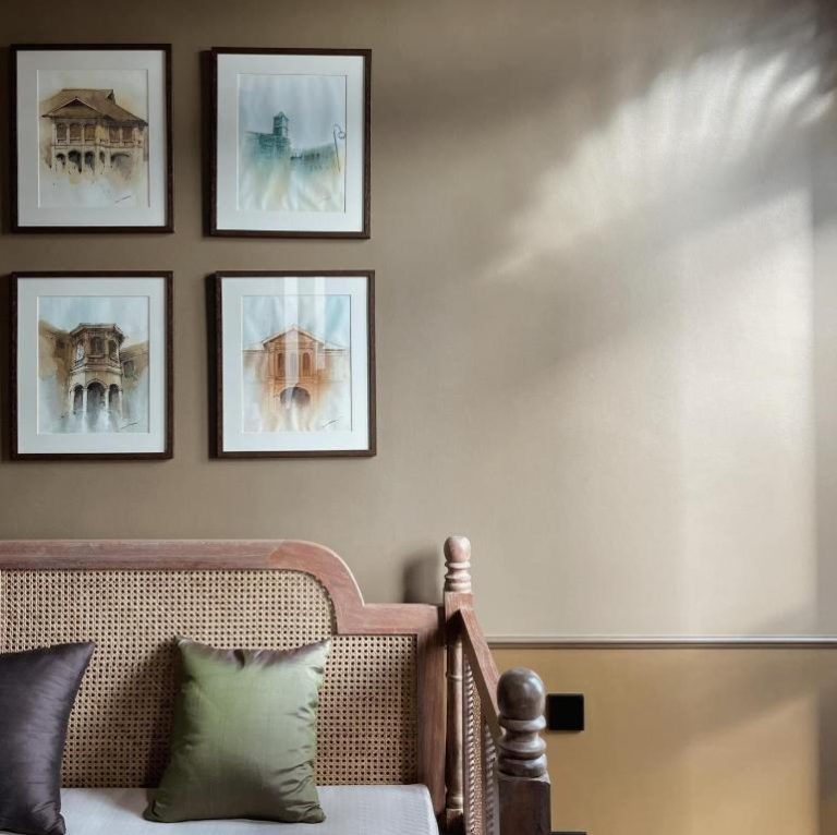 Habitación del Hotel Verdigris con cama de madera y ratán, cojines verdes y cuadros de acuarela arquitectónica