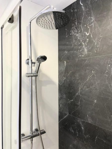 Ducha de lluvia con columna cromada y revestimiento de mármol negro en Vigablanca Apartments