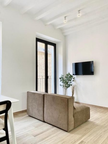 Salón moderno con sofá marrón, televisión y balcón en Vigablanca Apartments