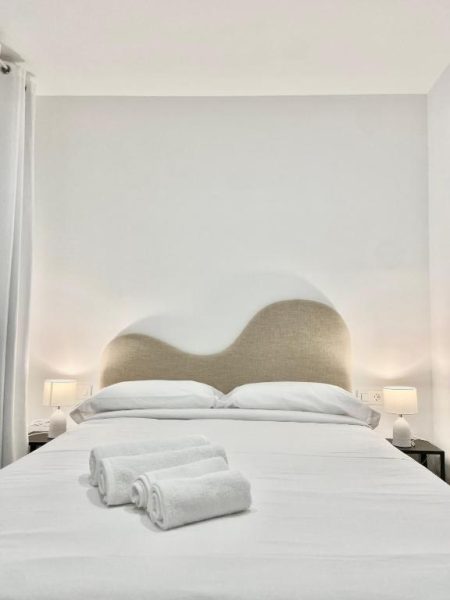 Habitación doble con cama matrimonial blanca y cabecero decorativo en Vigablanca Apartments