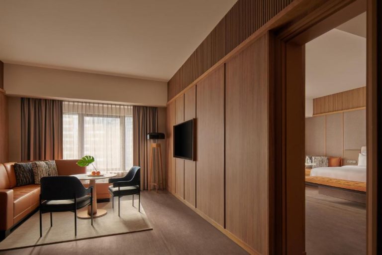 Suite del Amara Singapore con salón moderno, sofá marrón y acceso a dormitorio separado