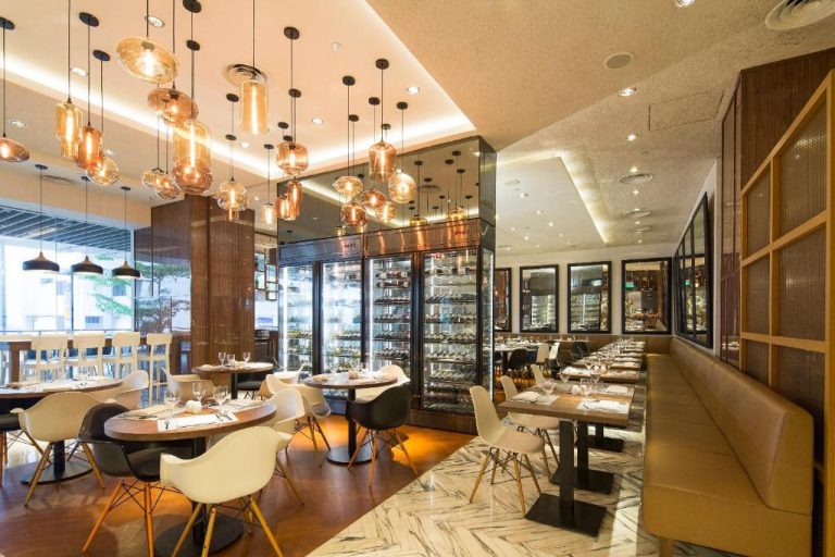 Restaurante interior del Amara Singapore con lámparas colgantes doradas, bodega y mesas elegantemente decoradas