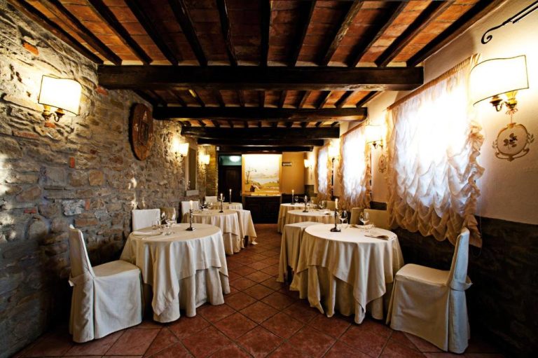 Elegante restaurante rústico con mesas vestidas en blanco y vigas de madera en Relais La Corte dei Papi