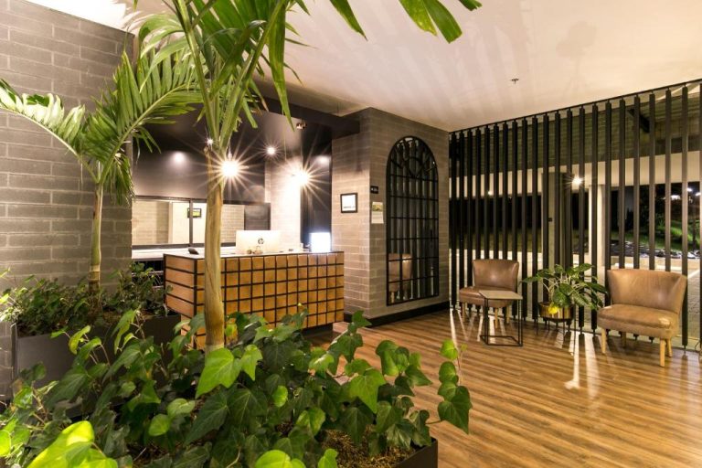 Recepción del Loma Verde Aparthotel con plantas tropicales, suelo de madera y zona de espera con sillones