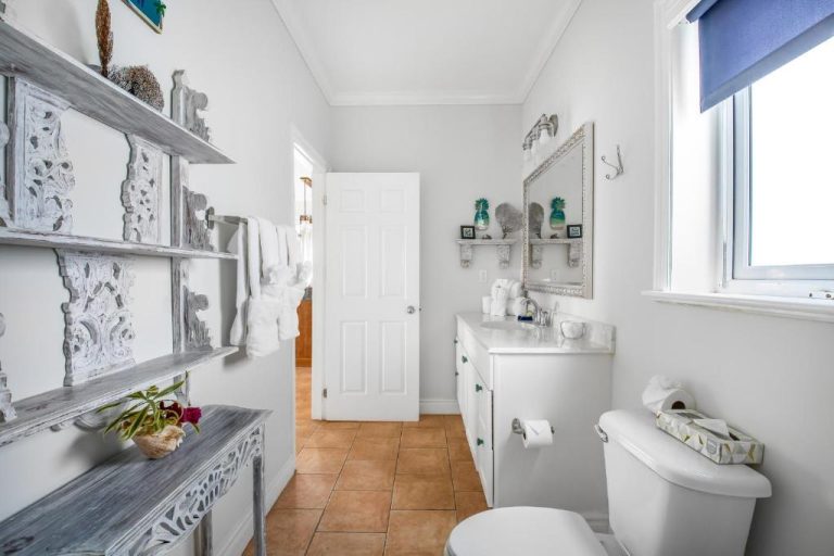 Baño blanco con decoración costera y estanterías de madera en Pineapple Fields Hotel
