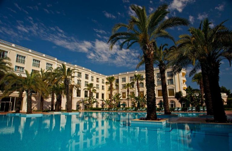 Piscina exterior rodeada de palmeras con vistas a la fachada del IC Hotels Airport en Antalya