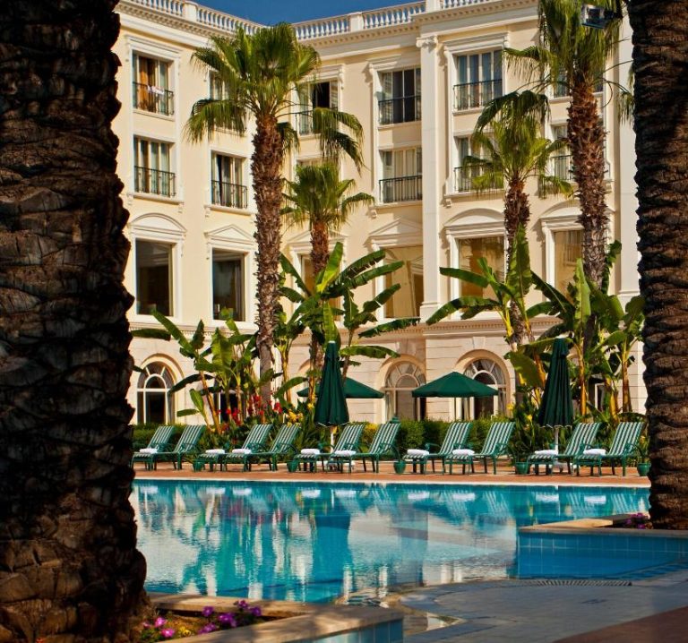 Piscina exterior con tumbonas y palmeras del IC Hotels Airport rodeada de exuberante vegetación tropical