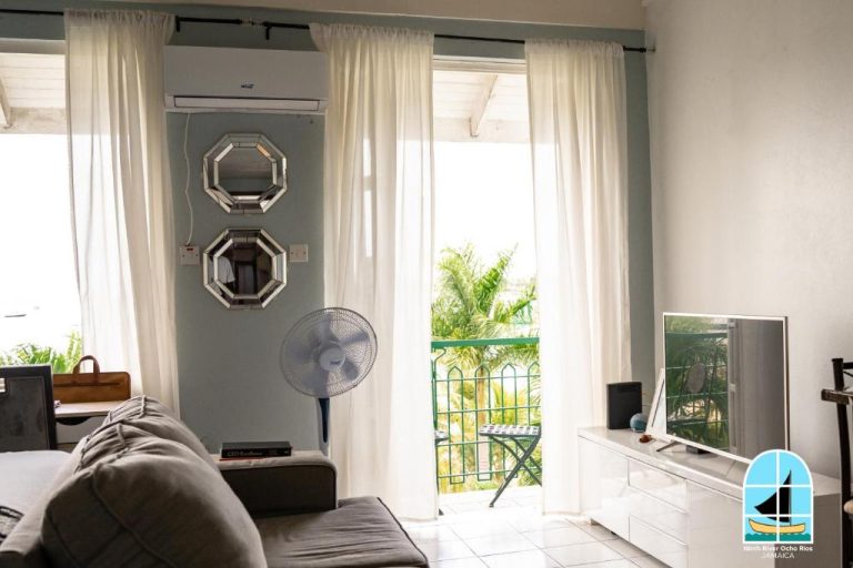 Salón con sofá y televisión con acceso a balcón tropical en Ninth River Ocho Rios Jamaica