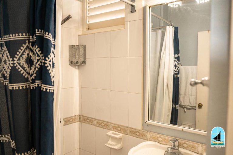 Baño con ducha, lavabo y cortina azul decorativa en el hotel Ninth River Ocho Rios Jamaica