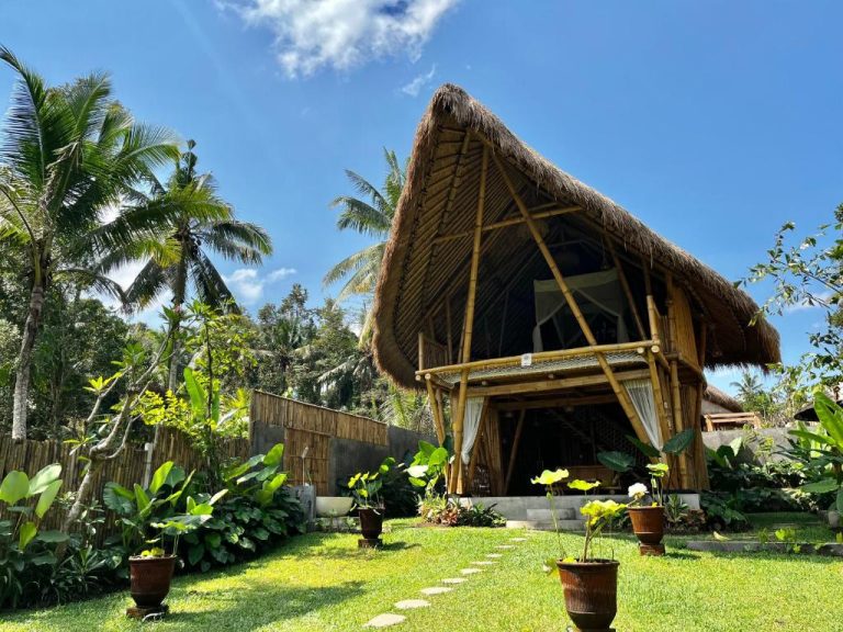 Cabaña de bambú con techo de paja rodeada de palmeras tropicales en Pitu Punggul Village Escape